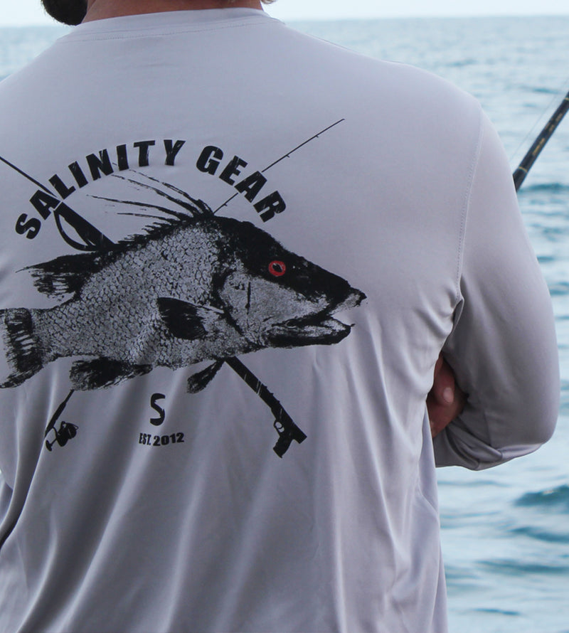 Salinity Gear performance SPF 50 sun protection dri-fit long sleeve fishing shirt. Grey shirt with screen printed ( reel vs steel ) hogfish fish rubbing or gyotaku design with crossed fishing pole and speargun on back. Screen printed distressed Salinity logo on front.